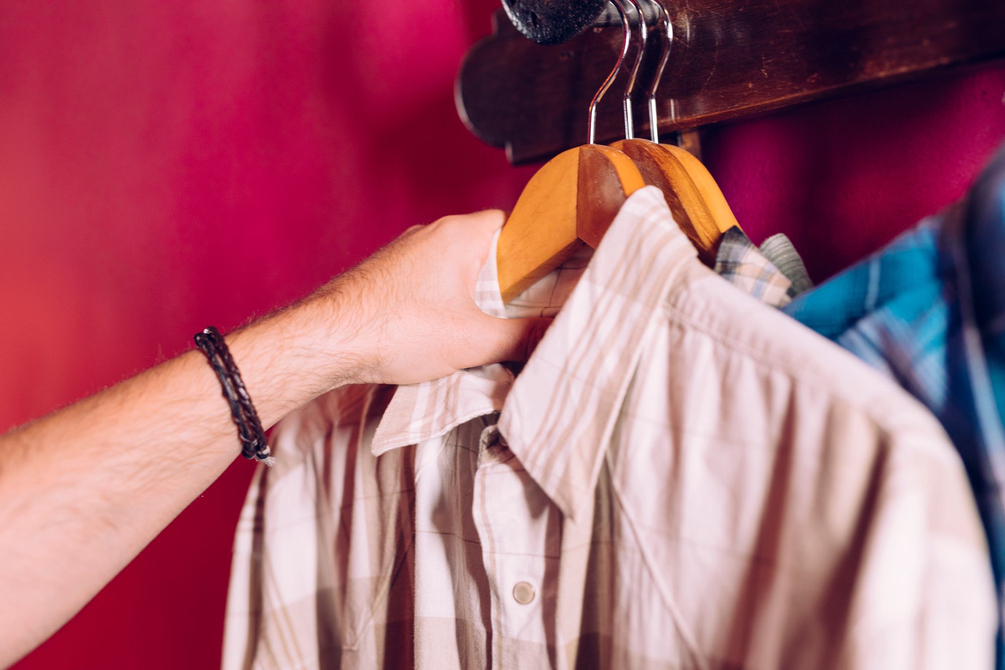 man-s-hand-taking-coat-hanger-shirt-from-rack-hook-red-wall